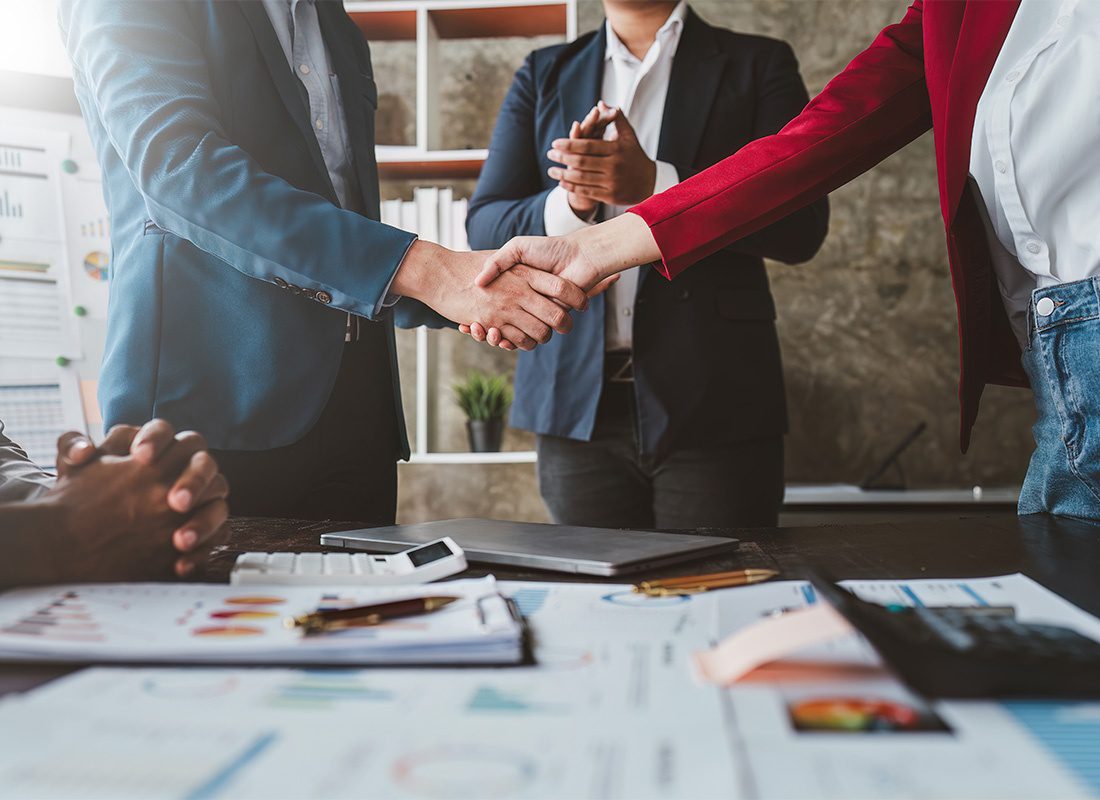 About Our Agency - View of a Small Team of Employees Shaking Hands and Celebrating Success in a Conference Room in the Office During a Business Meeting