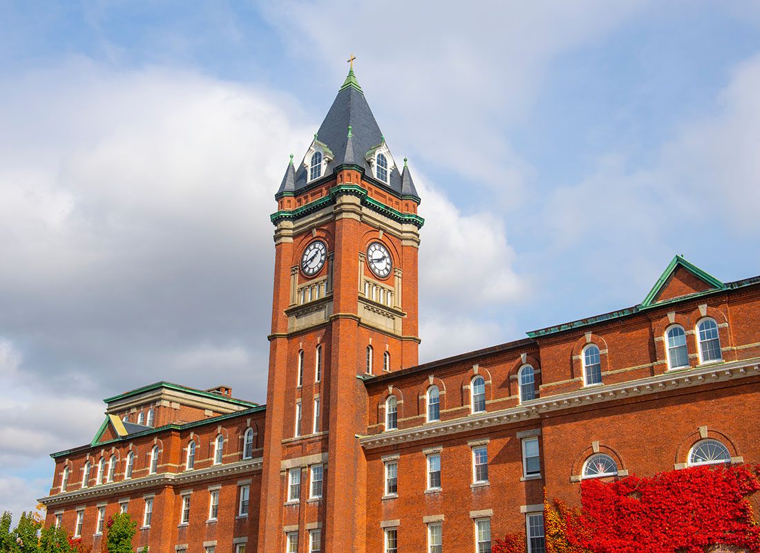 How It All Began - View of a Clock Tower on a College Campus Building Against a Cloudy Blue Sky with a Red Tree in the Front in Central Massachusetts