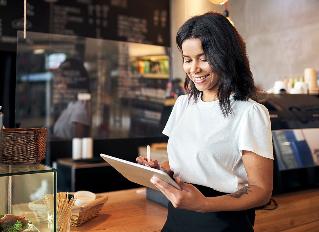 Client Service - Portrait of a Cheerful Young Female Restaurant Owner Standing in Front of the Counter While Using a Tablet